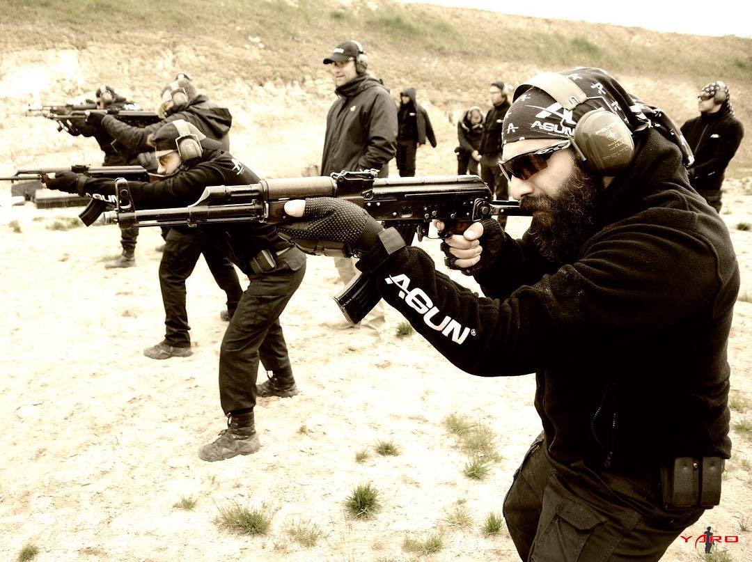 A line of trainees firing rifles on the outdoor range while instructors observe