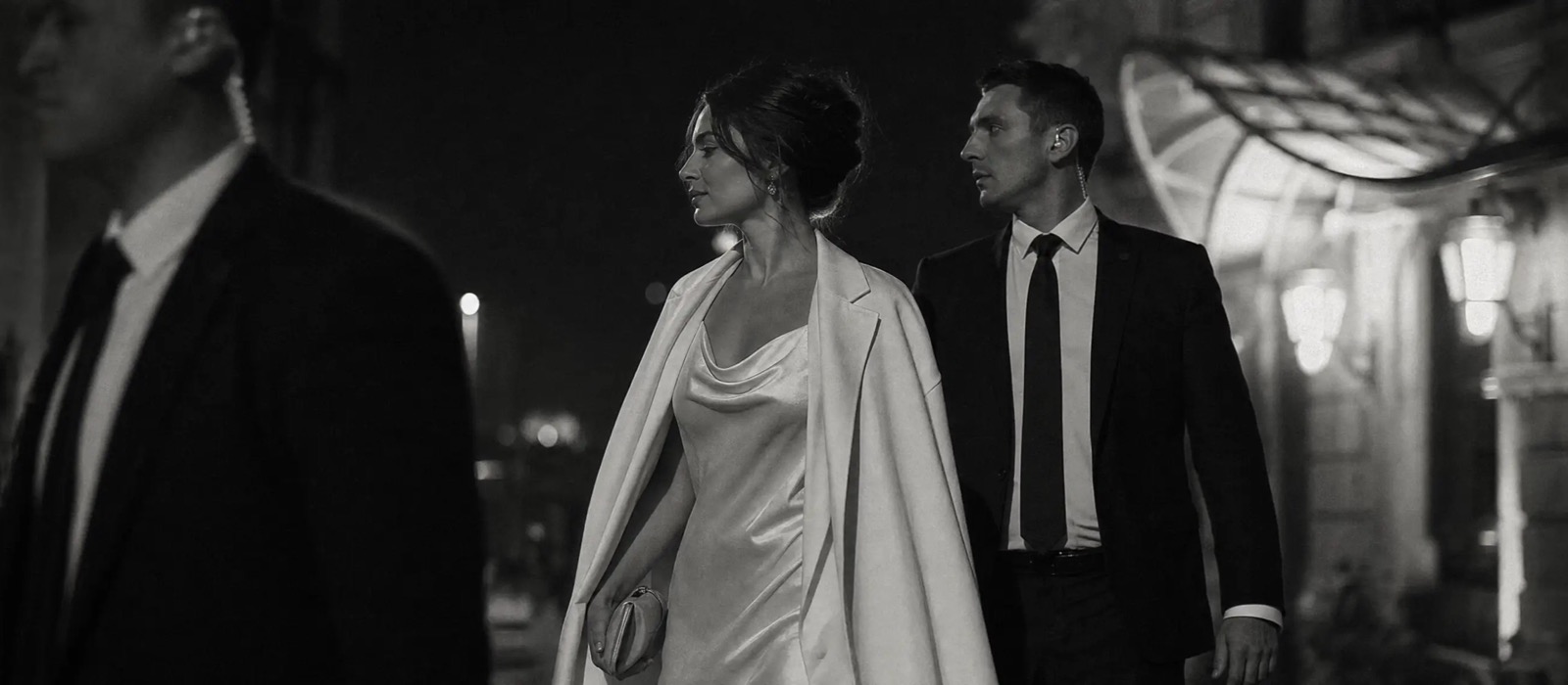 Close protection officer escorting a client in an evening gown outside a hotel entrance at night