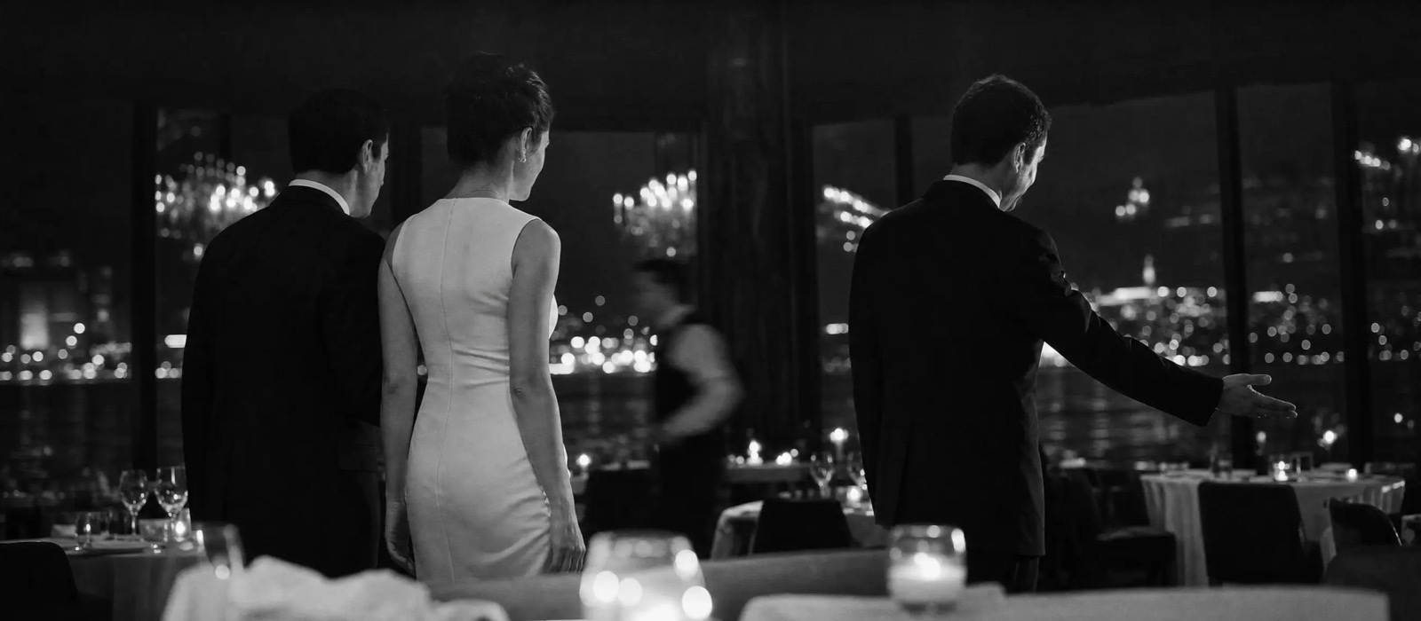 Maitre d' leading a couple to their reserved table in a restaurant overlooking the city lights
