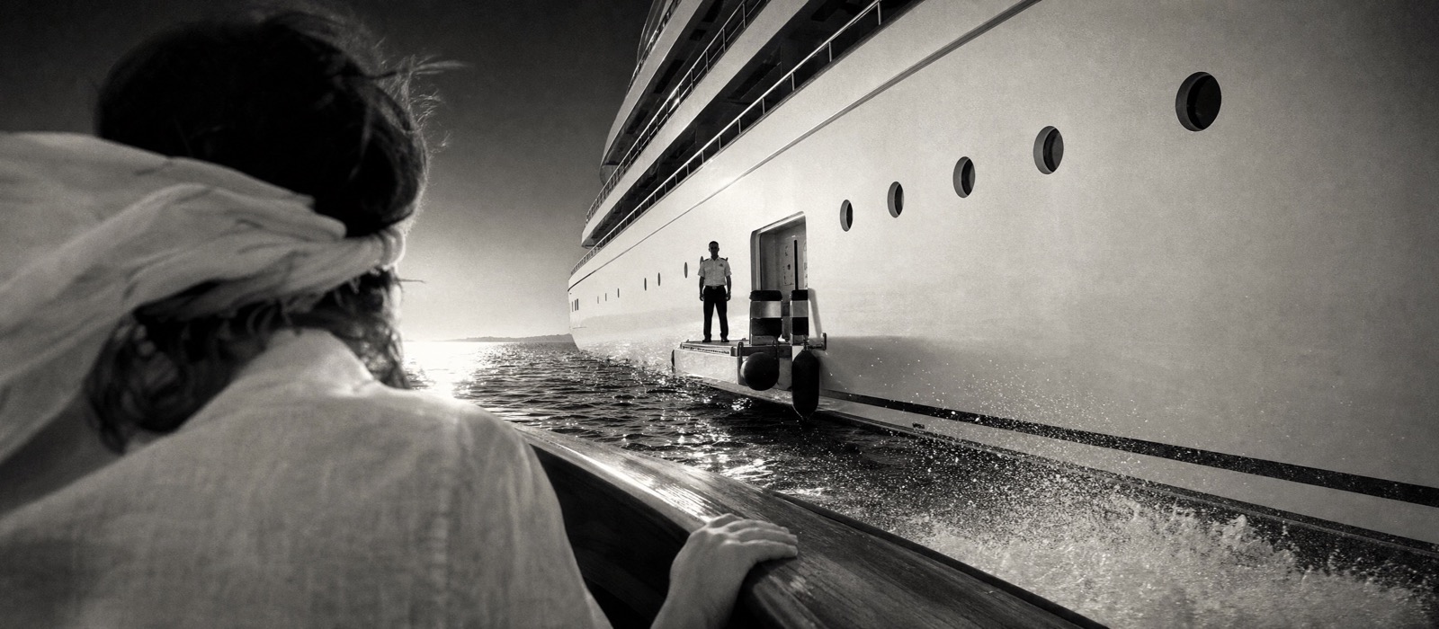 View from a tender approaching a chartered mega yacht, a crew member waiting at the boarding platform